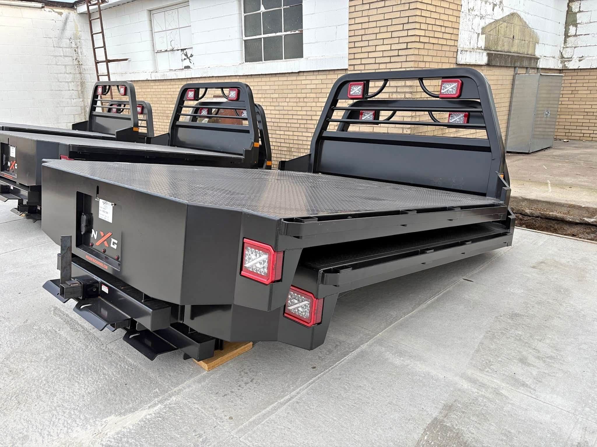 NXG XFD steel flatbed body in black powder coat, rear three-quarter view showing the diamond plate deck, built-in headache rack, and LED tail lights